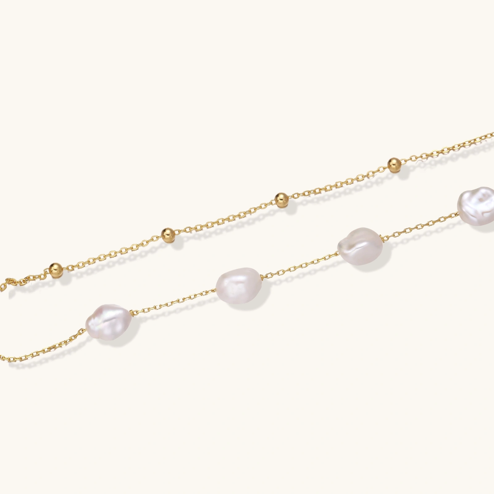 baroque pearl layered bracelet Double-strand gold bracelet with irregular baroque pearls and smooth freshwater pearls on cream background.