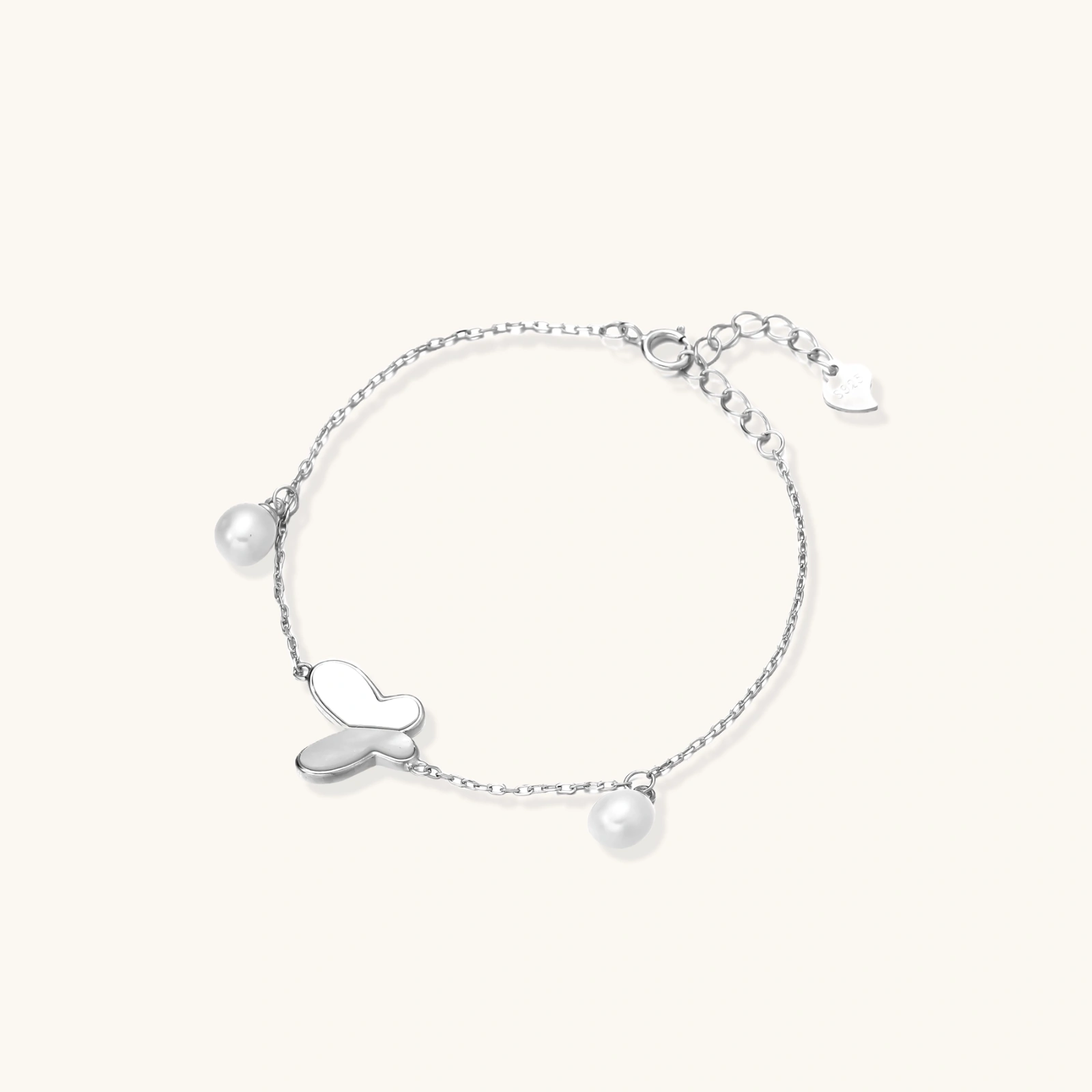 242255391770497024.webp Delicate rhodium-plated silver chain bracelet with butterfly charm and two freshwater pearls on cream background