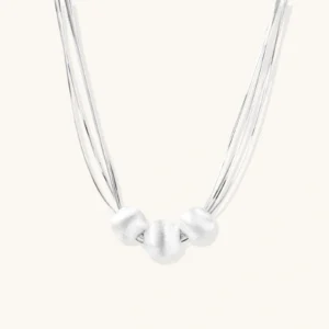 Sterling silver multi-strand necklace with three brushed round beads on cream background