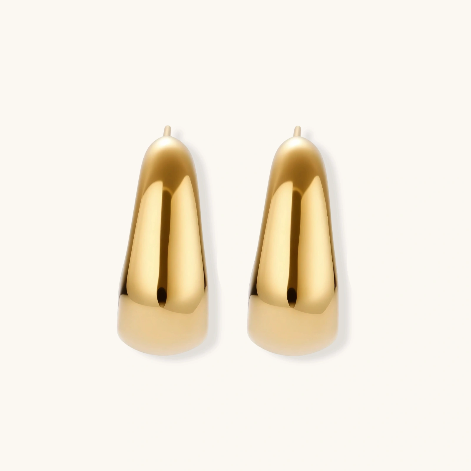 260904295254609920.webp Close-up of curved gold-plated huggie earrings with sculptural design on white background, showing polished finish.