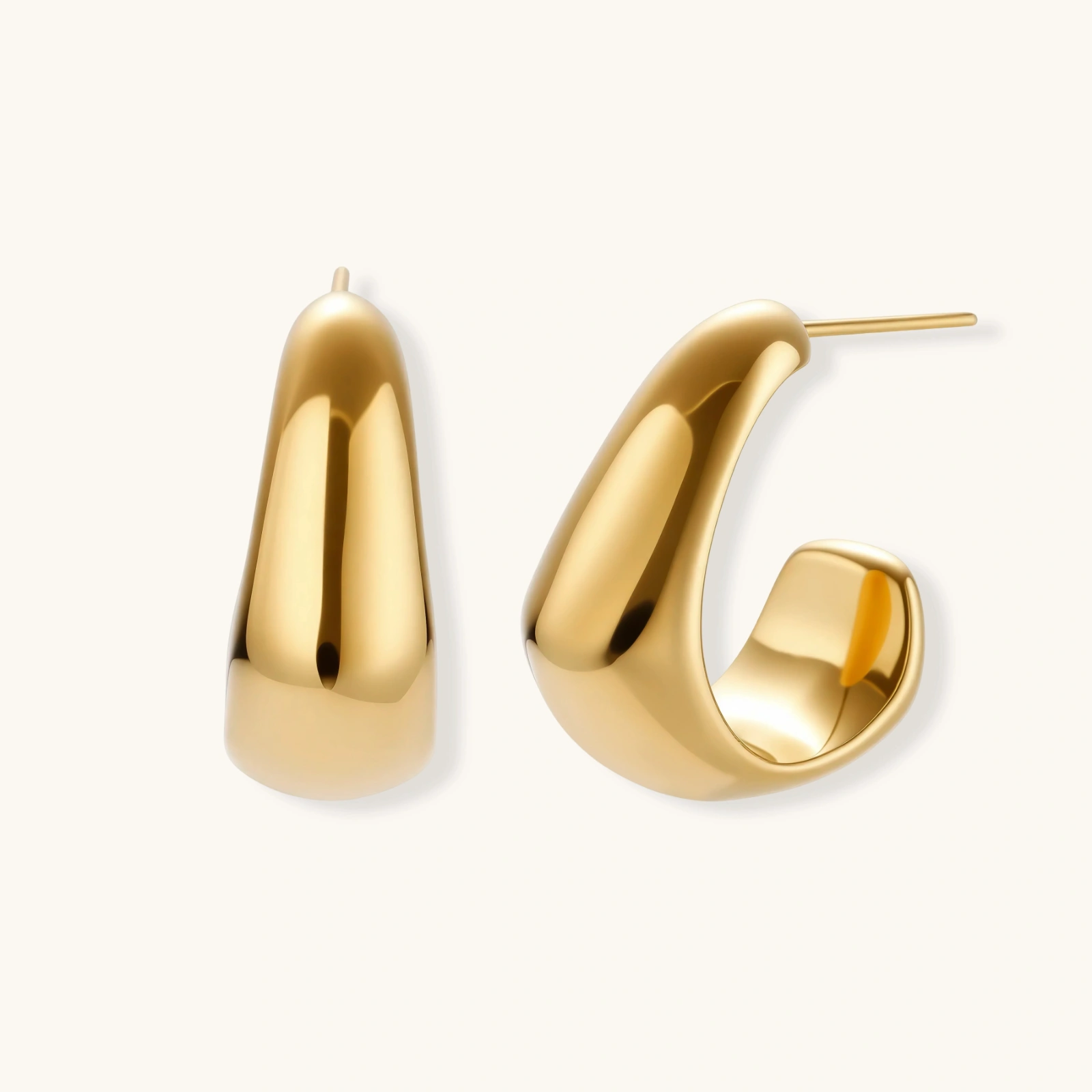 260904295531433984.webp Close-up of curved gold-plated huggie earrings with sculptural design on white background, showing polished finish.