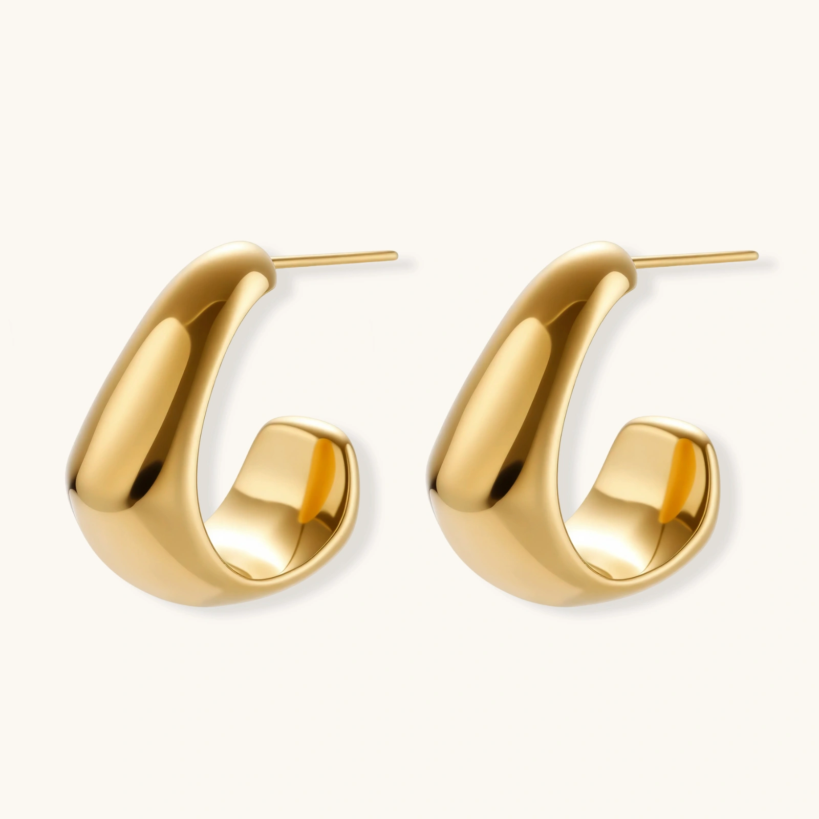 260904323440332800.webp Close-up of curved gold-plated huggie earrings with sculptural design on white background, showing polished finish.