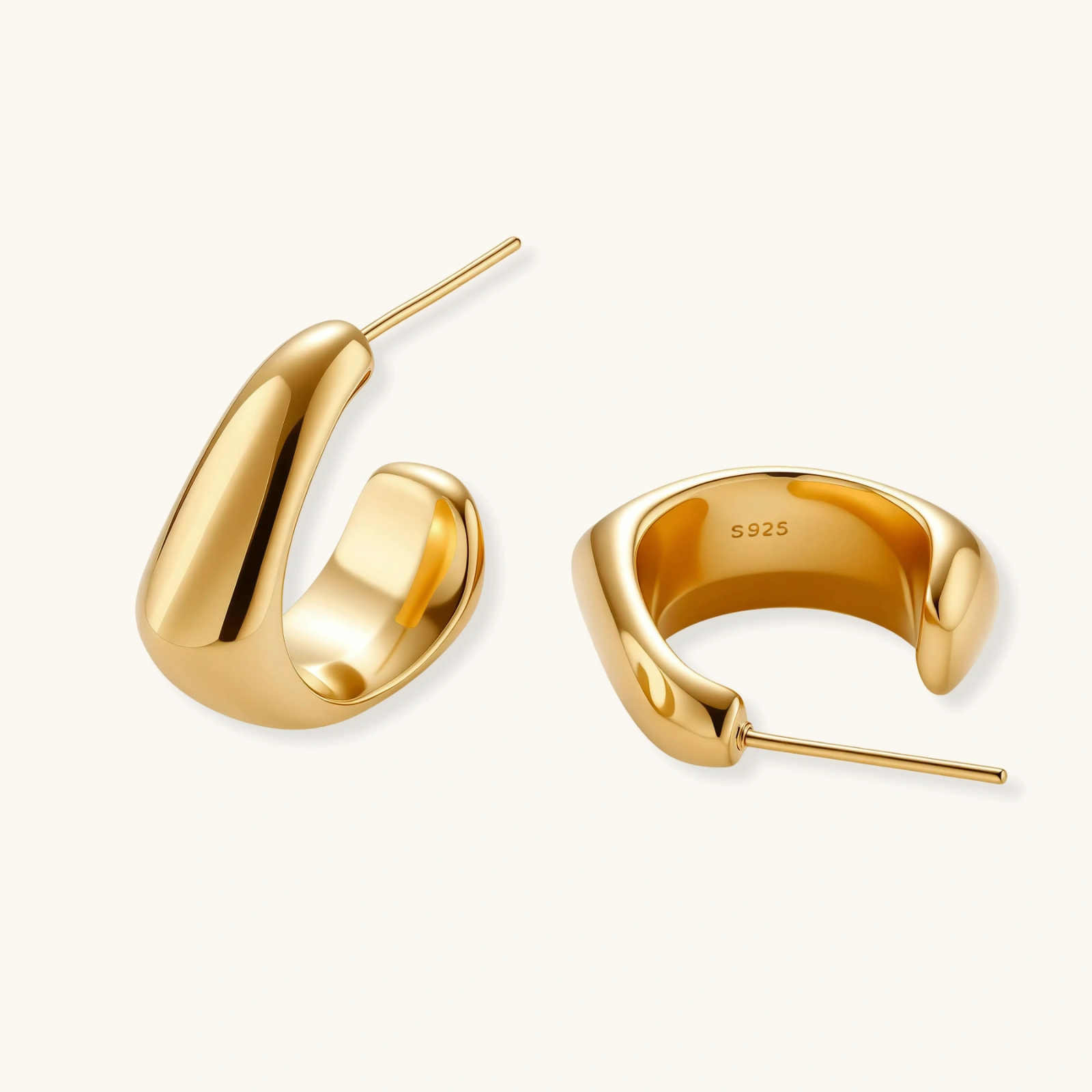 260904326841913344.webp Close-up of curved gold-plated huggie earrings with sculptural design on white background, showing polished finish.