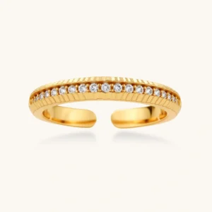 Adjustable gold-plated ring with row of sparkling crystals on ribbed band, shot against cream background