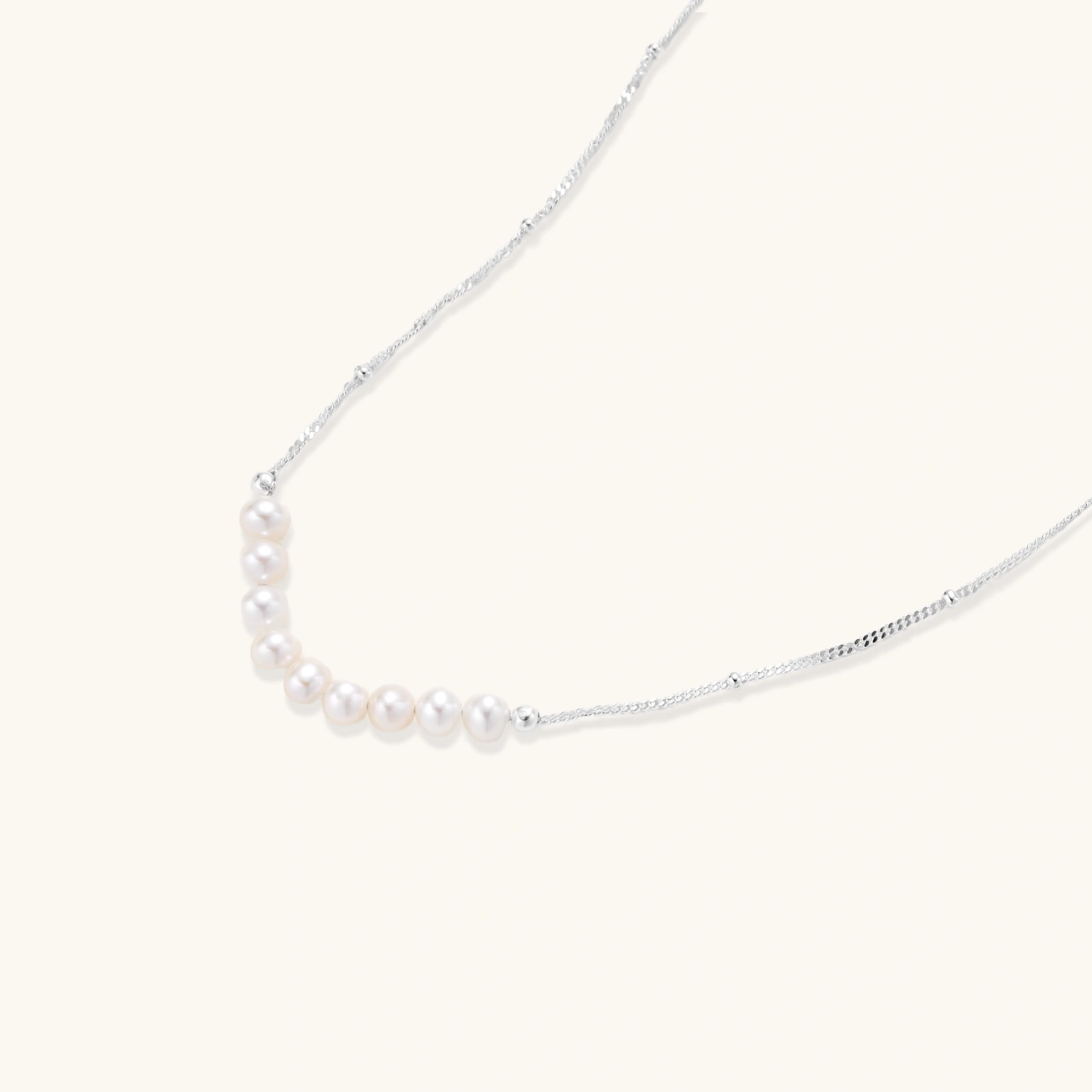 242260115507015680.webp Delicate sterling silver chain necklace with small freshwater pearls arranged in a curved smile arc on cream background.