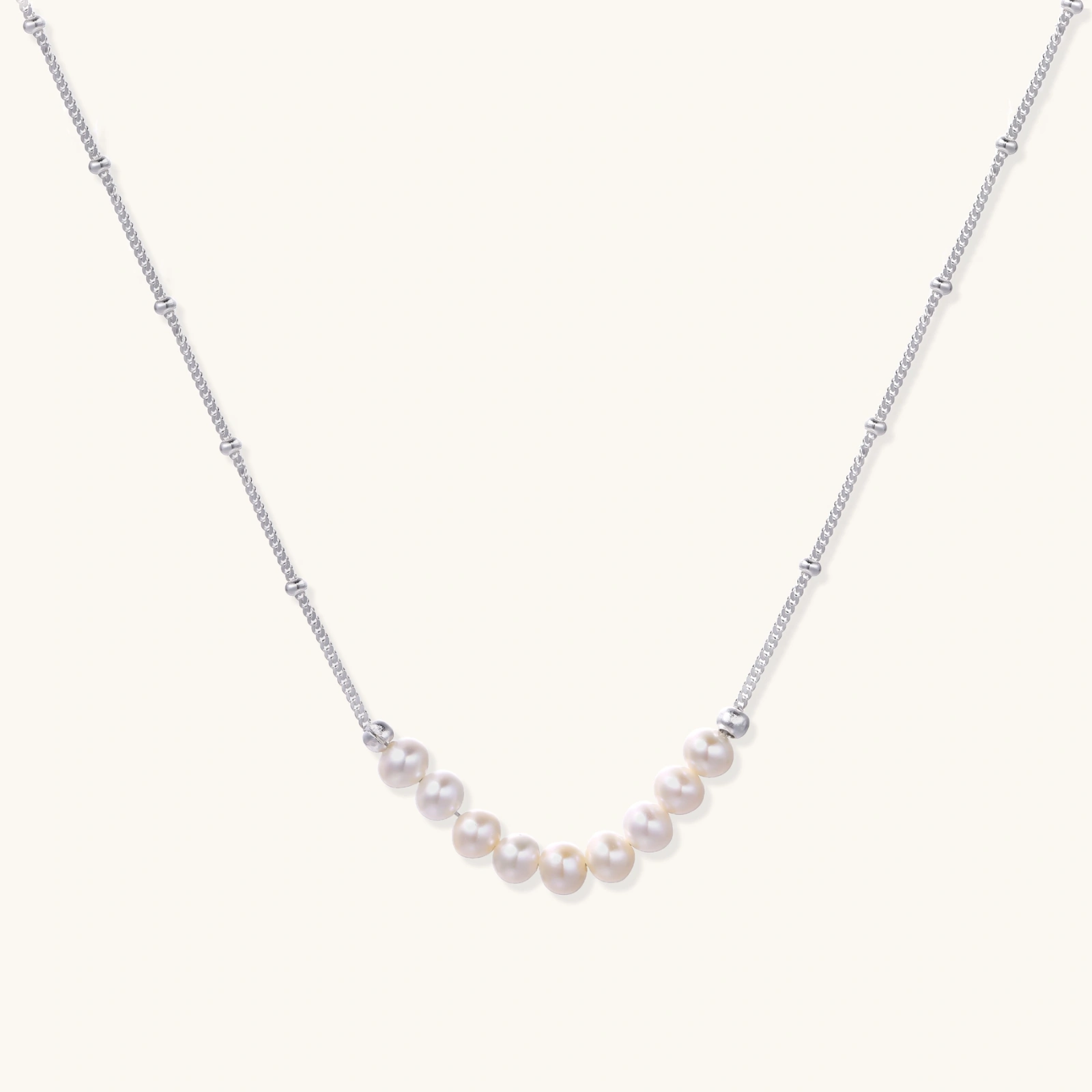 242260116178104320.webp Delicate sterling silver chain necklace with small freshwater pearls arranged in a curved smile arc on cream background.