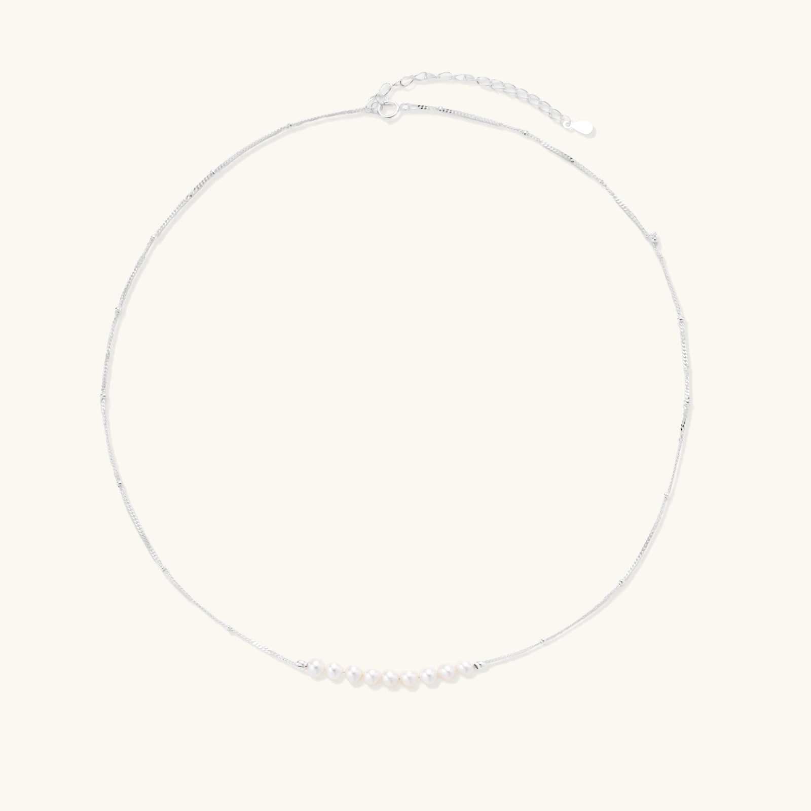 242260146909769728.webp Delicate sterling silver chain necklace with small freshwater pearls arranged in a curved smile arc on cream background.
