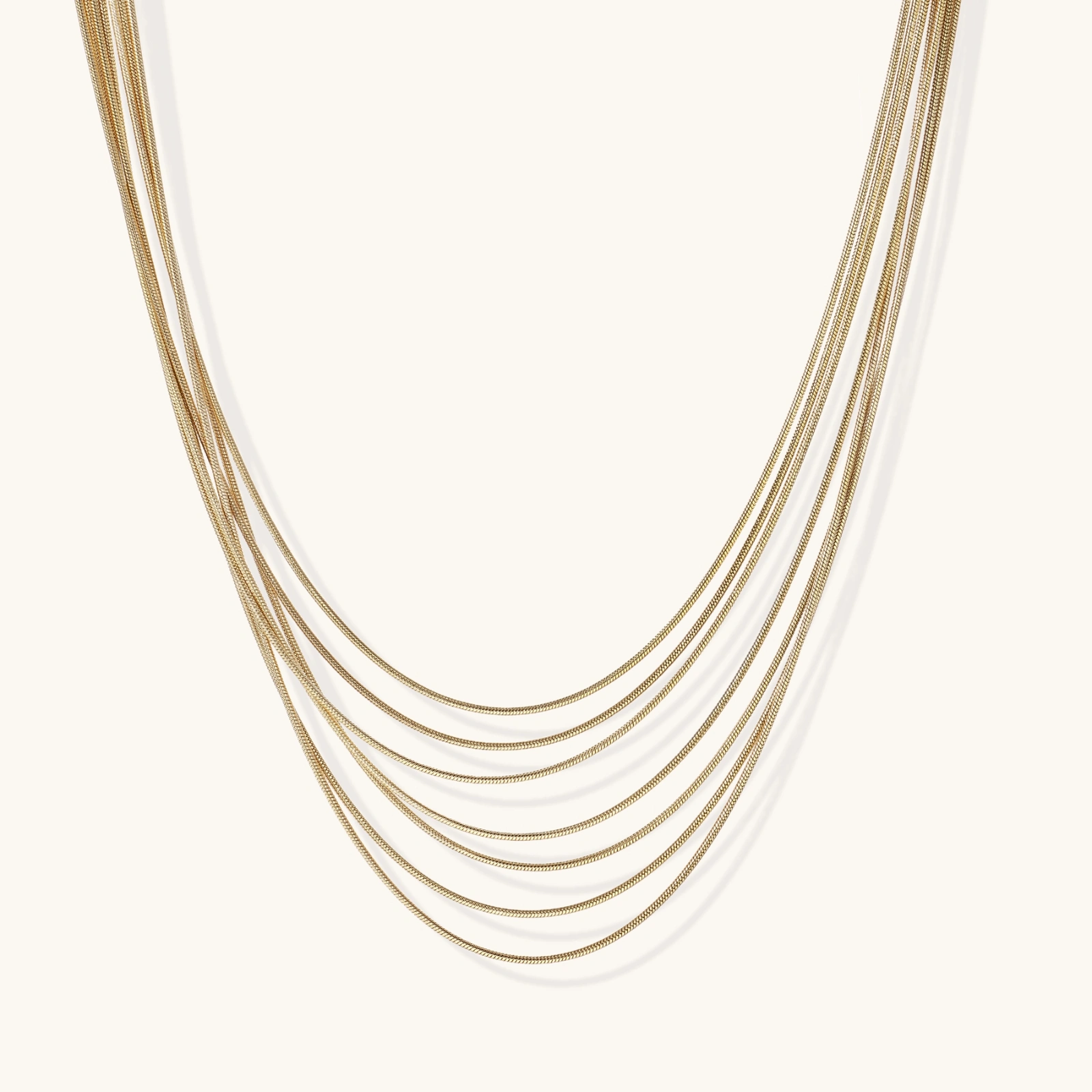 242421485129068544.webp Seven delicate gold-plated snake chains create an elegant layered necklace on a neutral background.