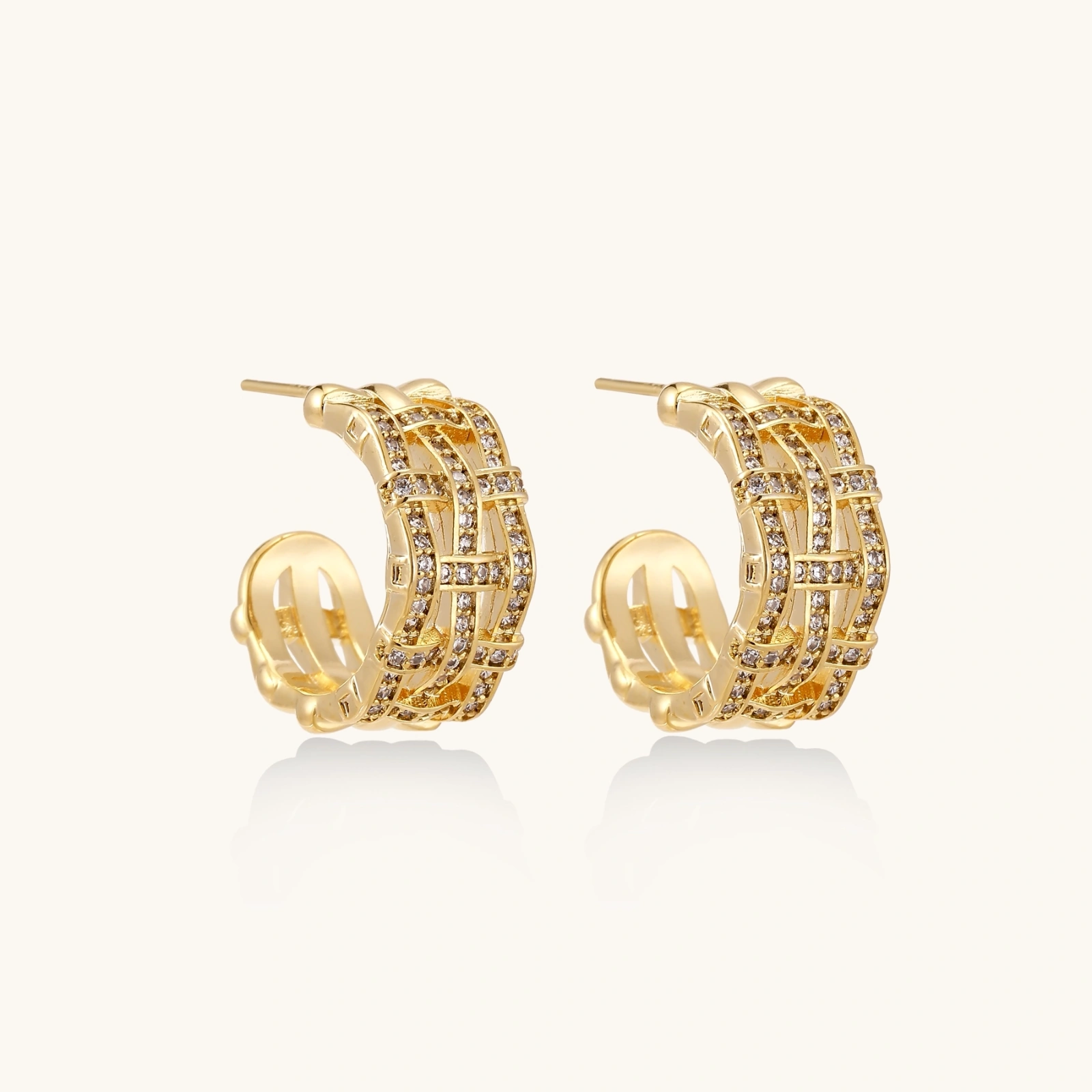 242422548072452096.webp Gold-plated geometric hoop earrings with basket-weave lattice design and pavé crystal accents on cream background